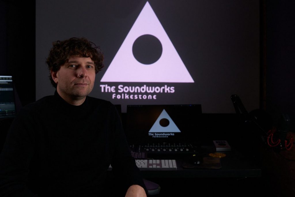 Michael Griggs sat in front of a mixing desk in the Soundworks studio with projected studio logo
