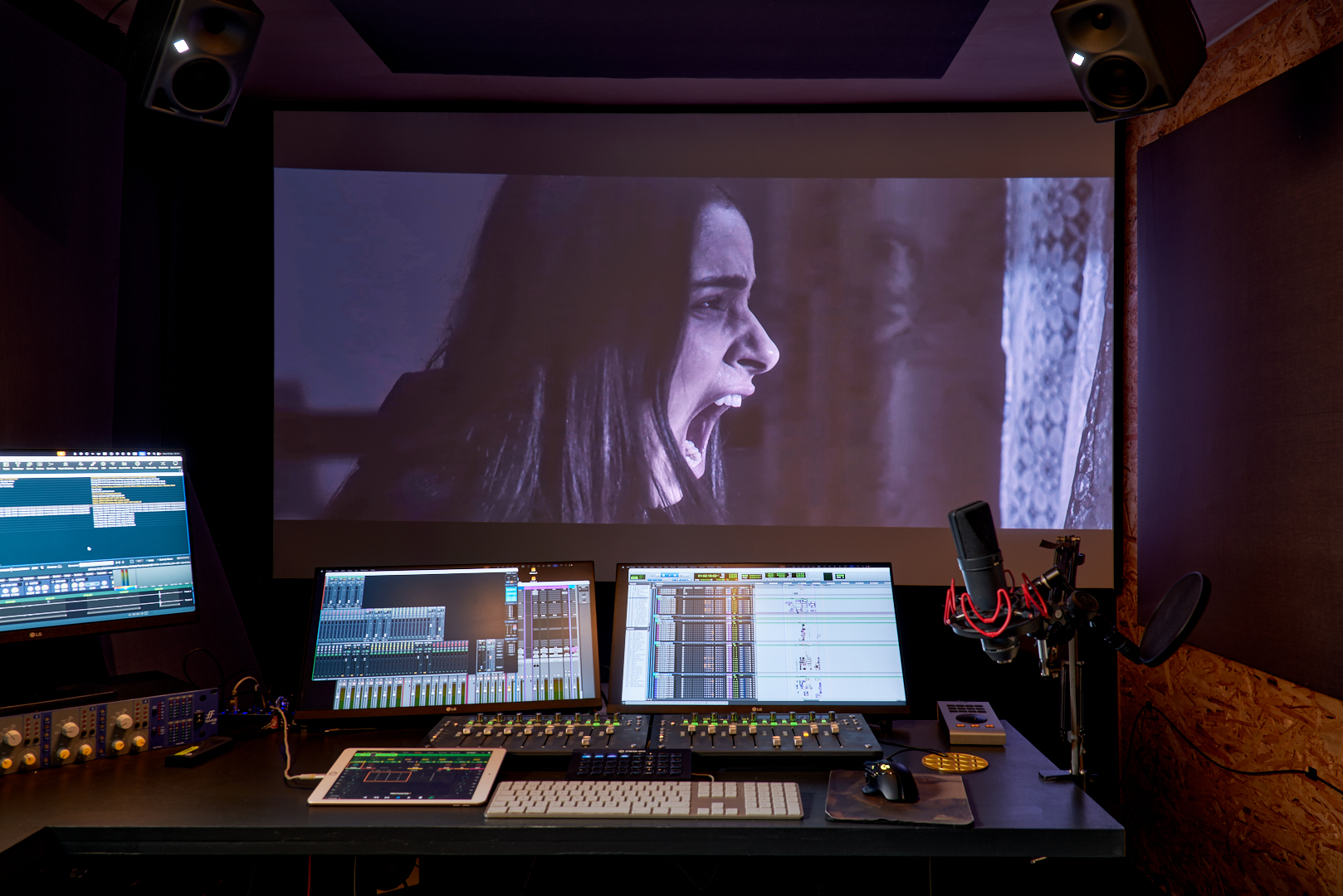 Audio mixing desk and computer setup with projected film image and studio microphone in a professional sound studio
